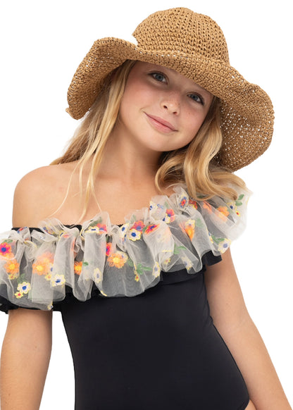 A young girl wearing a wide-brimmed straw hat and a black off-the-shoulder swimsuit with a sheer white ruffle decorated with colorful floral embroidery, set against a plain white background.