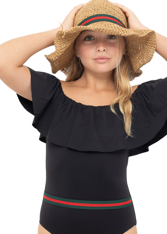 A young girl wearing a classic black swimsuit with a belt, matching straw hat, and sunglasses.